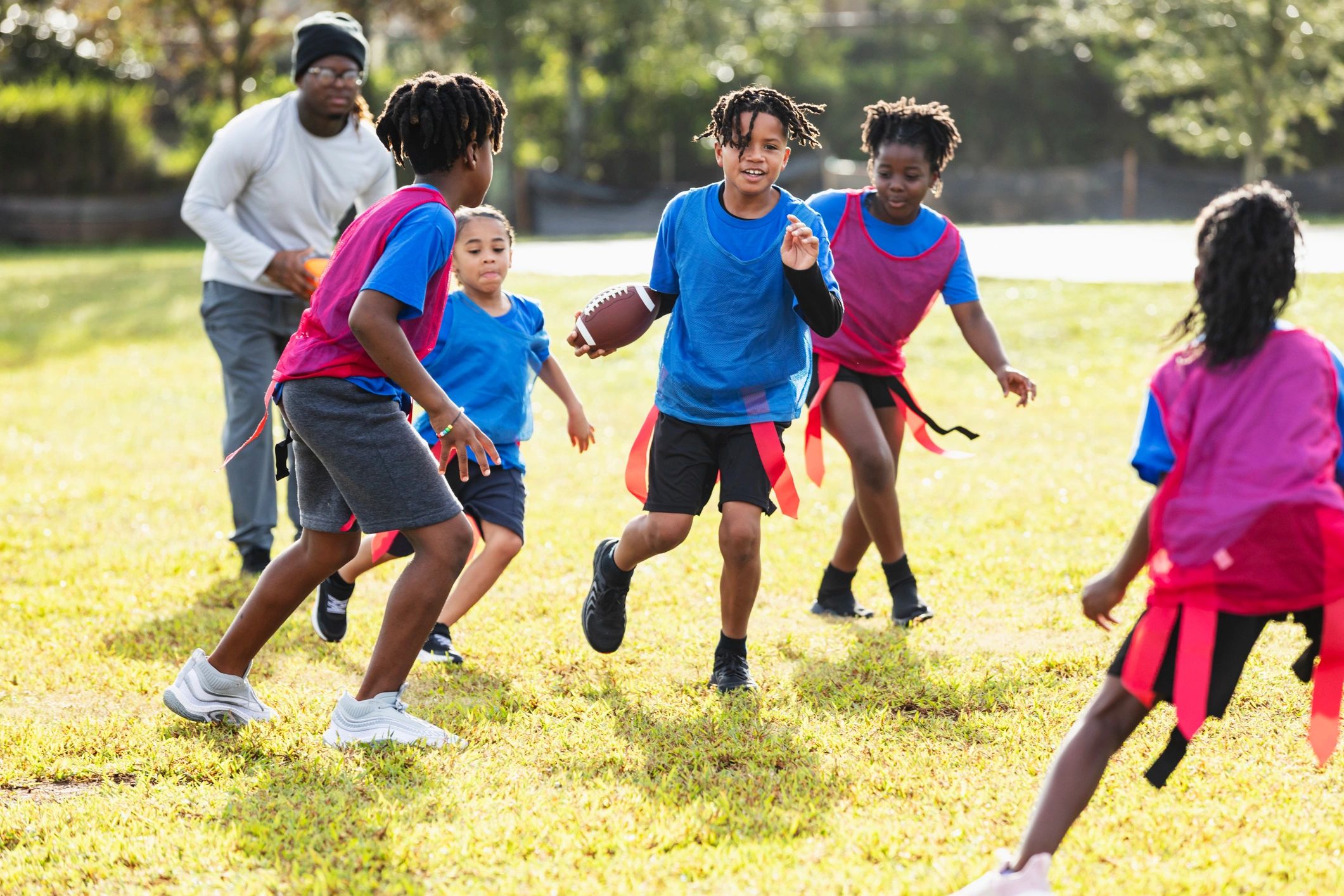Flag football maçında çocuklar ve kenarda oyunu izleyen bir antrenör/hakem.