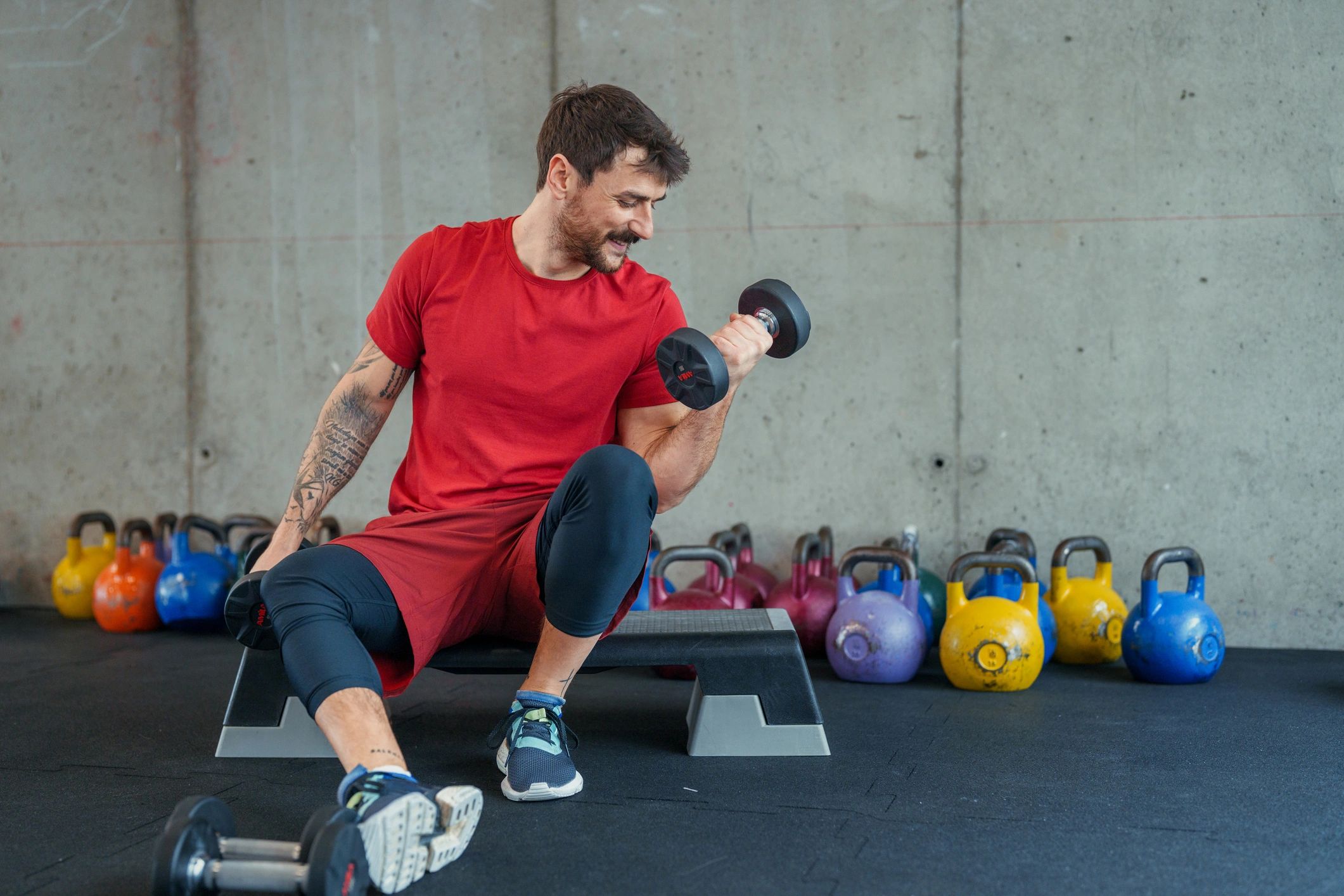 Kırmızı tişörtlü sporcu dumbbell ile kuvvet çalışıyor